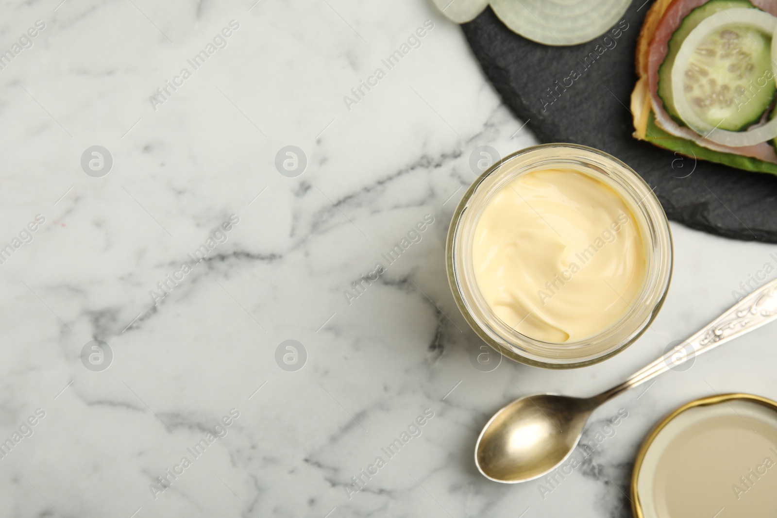 Photo of Jar of delicious mayonnaise near fresh sandwich on white marble table, flat lay. Space for text