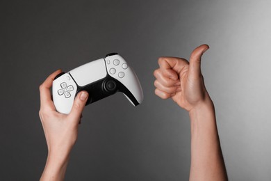 Woman with game controller showing thumbs up on grey background, closeup