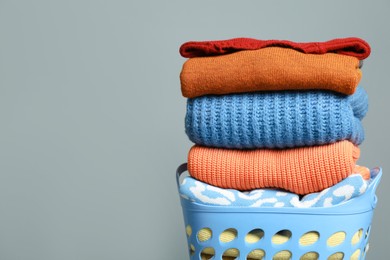Photo of Plastic laundry basket with clean clothes on grey background. Space for text