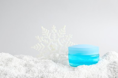 Photo of Jar of hand cream and decorative snowflake on snow against light background. Winter skin care