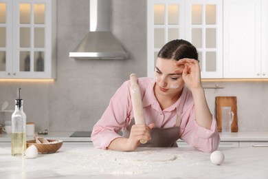Photo of Tired woman with soiled face holding rolling pin in messy kitchen