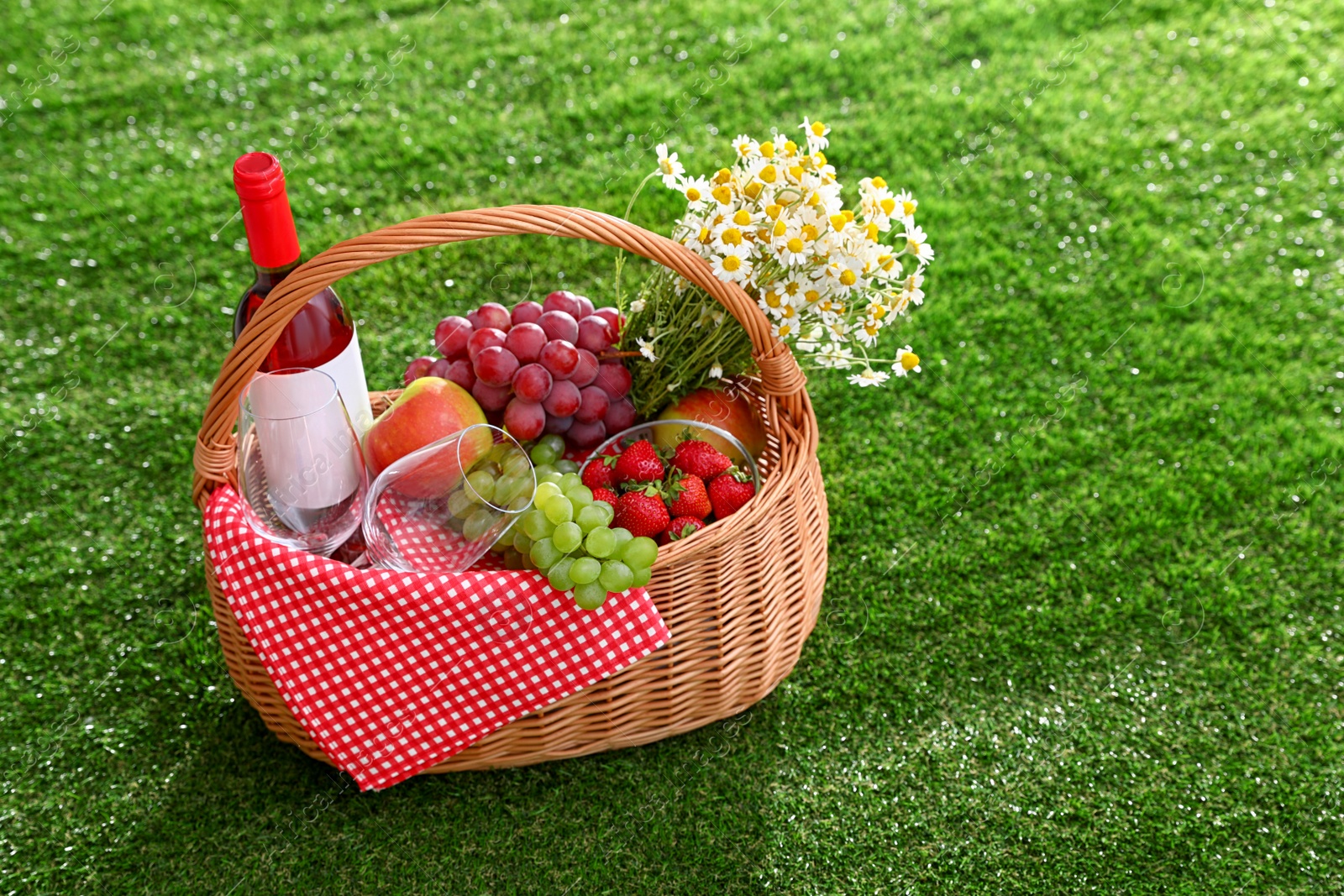 Photo of Picnic basket with wine and products on grass, space for text