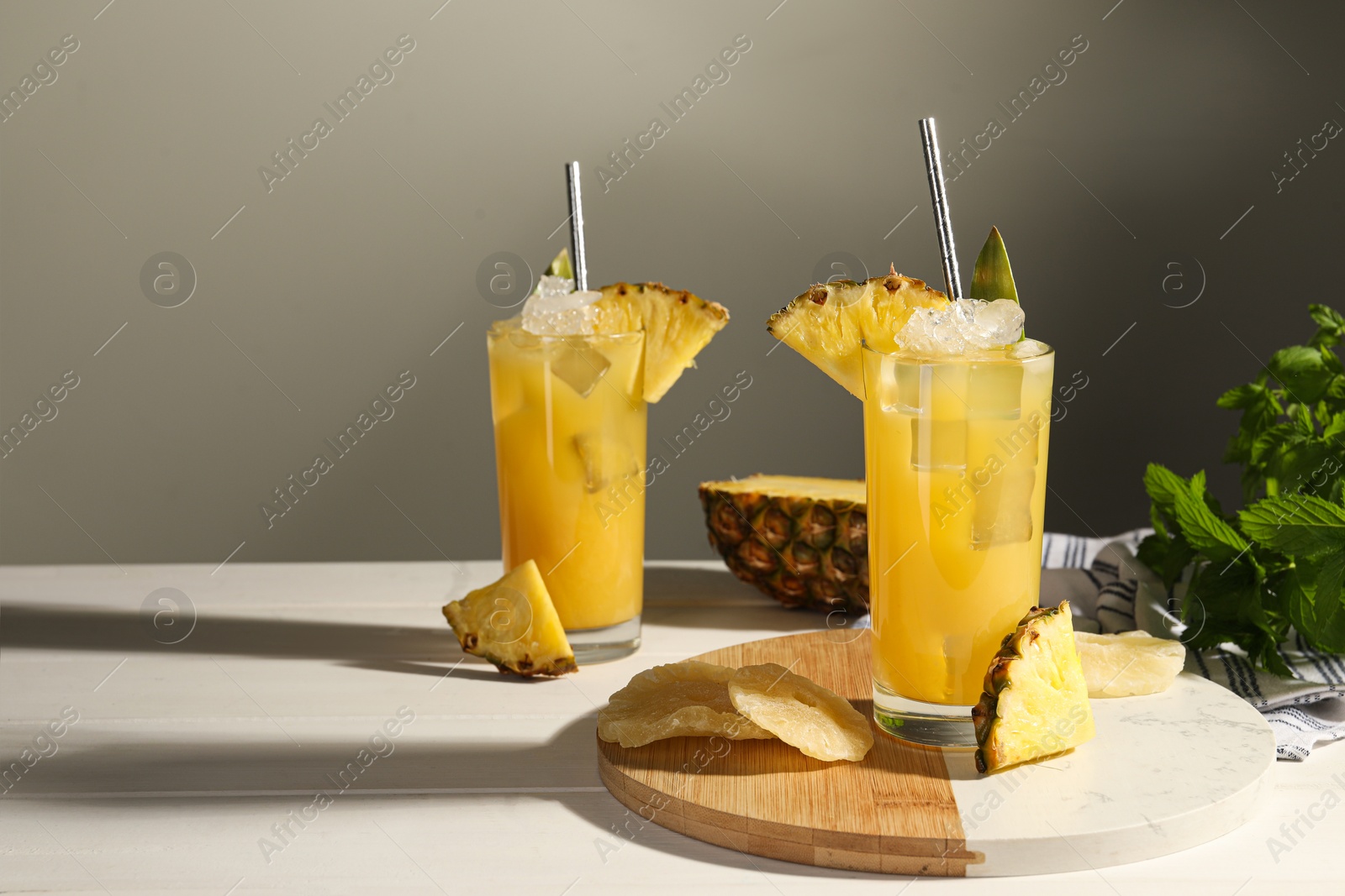 Photo of Tasty pineapple cocktails with ice cubes and delicious fruit on white wooden table, space for text