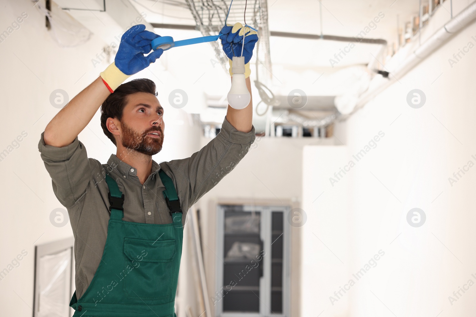 Photo of Electrician with insulting tape repairing ceiling lamp