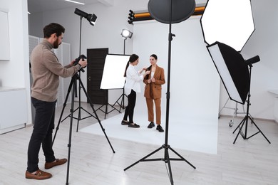 Professional photographer and stylist working with beautiful model in modern photo studio