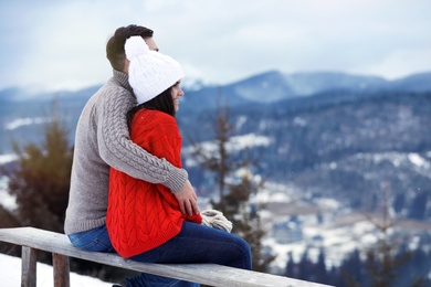 Couple sitting on bench and enjoying mountain landscape, space for text. Winter vacation