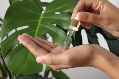 Photo of Woman applying cosmetic serum onto her hand near green plant, closeup