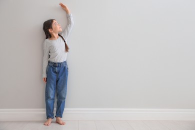 Photo of Little girl measuring her height near light grey wall indoors. Space for text