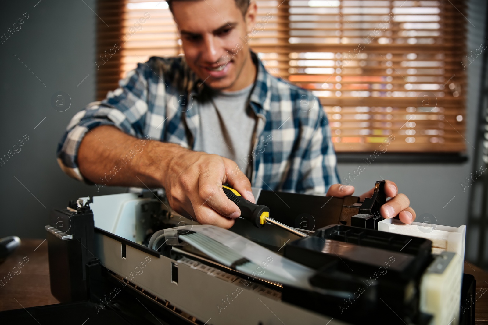 Photo of Repairman with screwdriver fixing modern printer in office, focus on hand