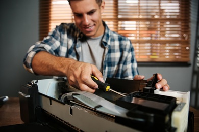 Photo of Repairman with screwdriver fixing modern printer in office, focus on hand