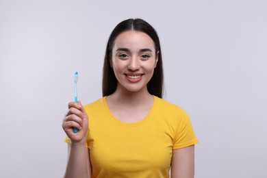 Happy young woman holding plastic toothbrush on white background