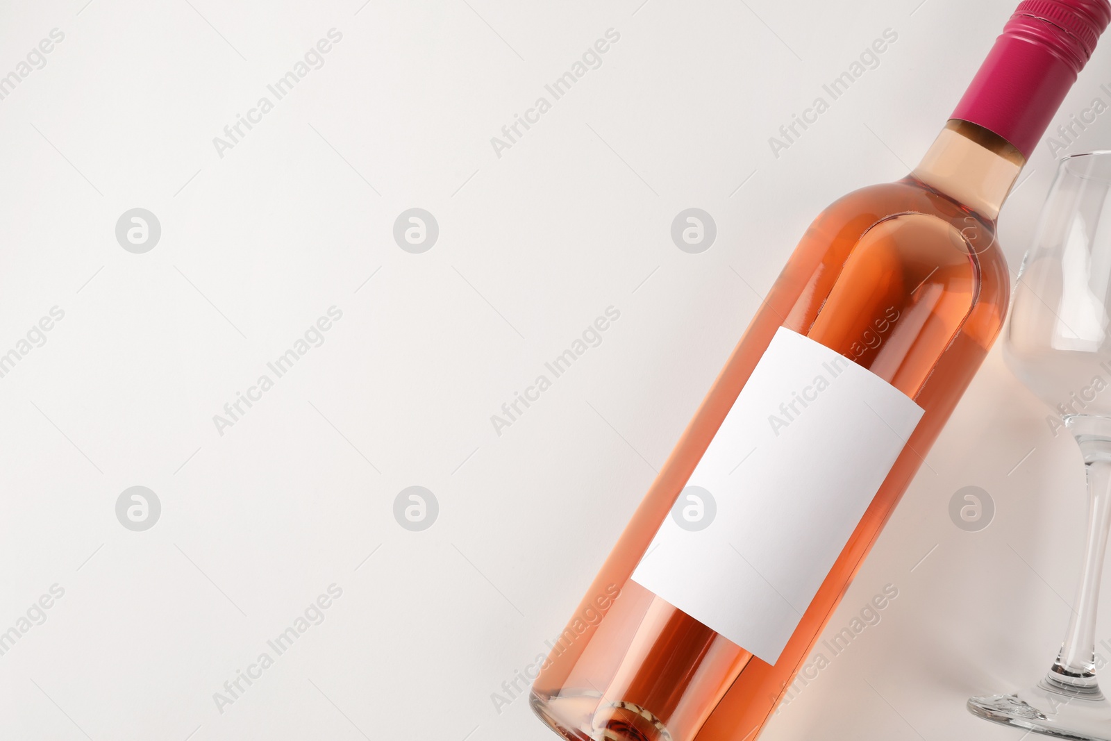 Photo of Bottle of tasty rose wine and glass on white background, flat lay. Space for text