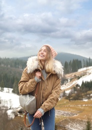 Young woman in warm clothes near snowy hill. Winter vacation