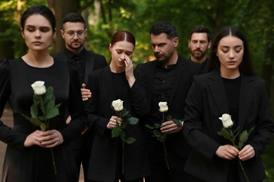 Photo of Funeral ceremony. Sad people with white rose flowers mourning outdoors