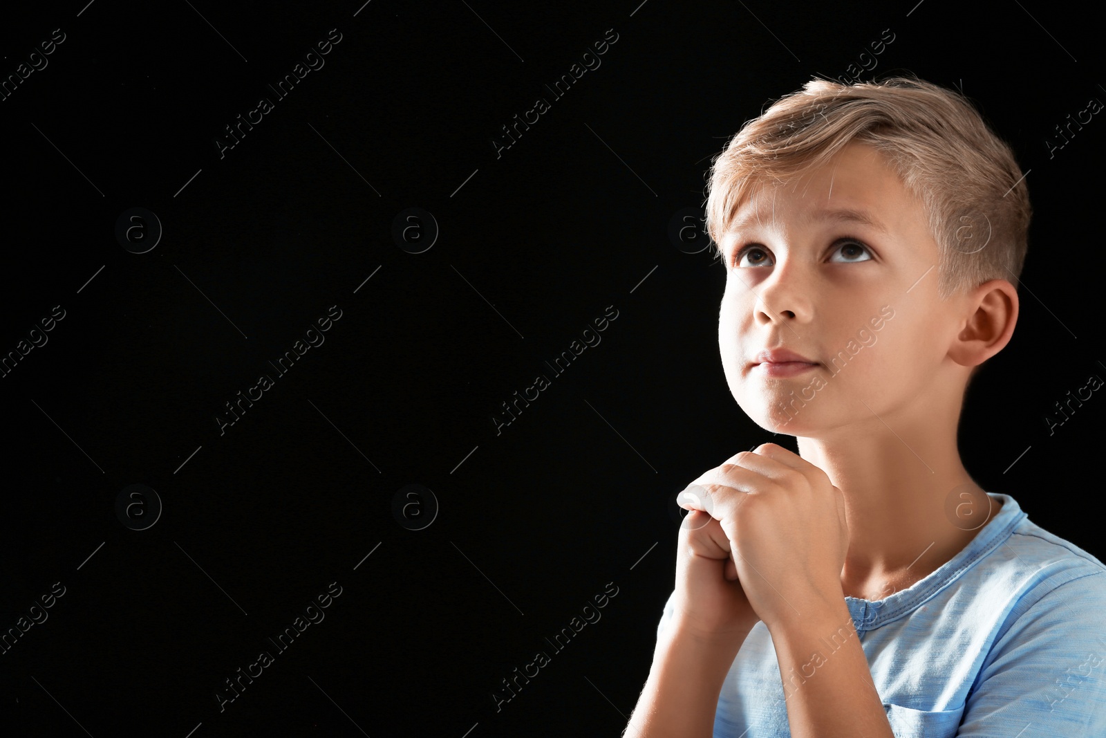 Photo of Little boy with hands clasped together for prayer on black background. Space for text