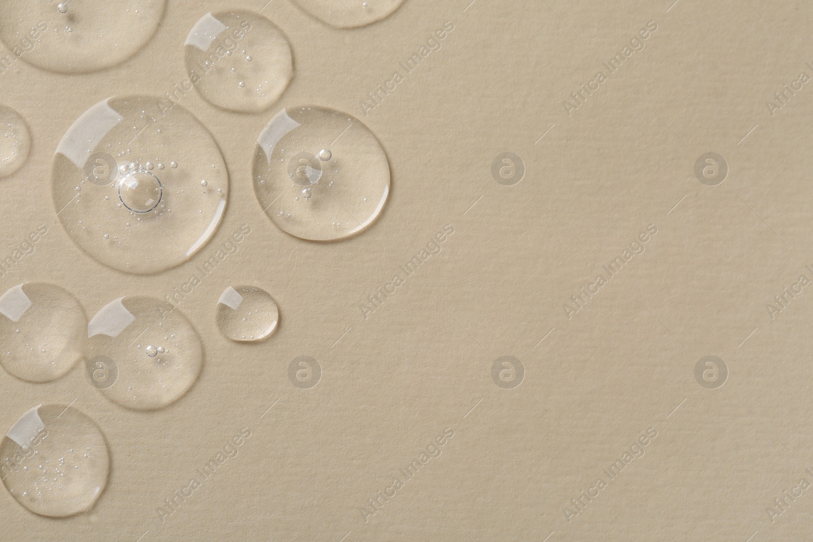 Photo of Drops of cosmetic serum on beige background, top view. Space for text