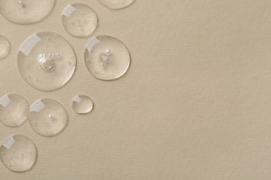 Photo of Drops of cosmetic serum on beige background, top view. Space for text