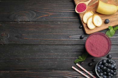 Photo of Fresh acai drink with berries and banana on dark wooden background, flat lay. Space for text