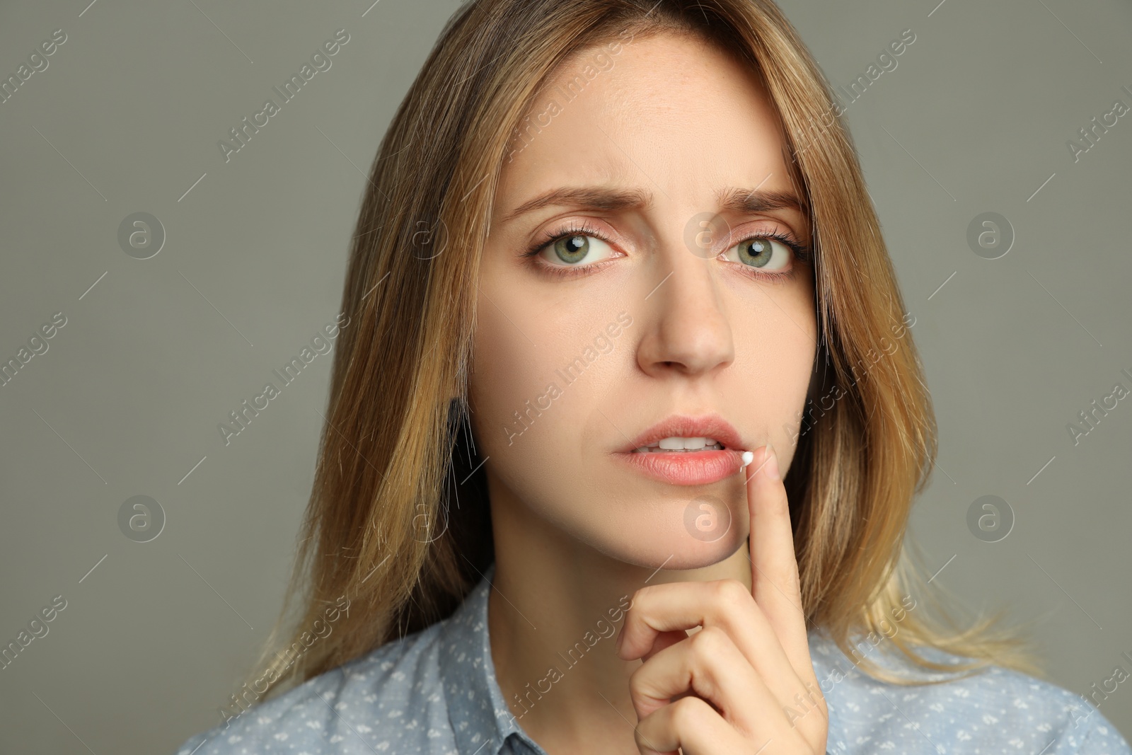 Photo of Woman with herpes applying cream onto lip against  light grey background