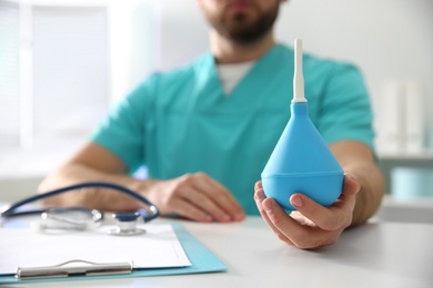 Photo of Doctor holding light blue enema at table in hospital, closeup
