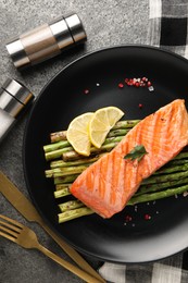 Tasty grilled salmon with asparagus, lemon and spices served on gray table, flat lay