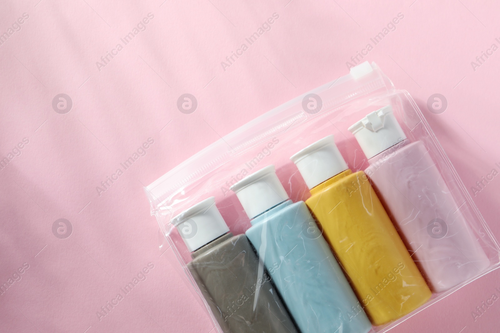 Photo of Cosmetic travel kit in plastic bag on pink background, top view. Space for text