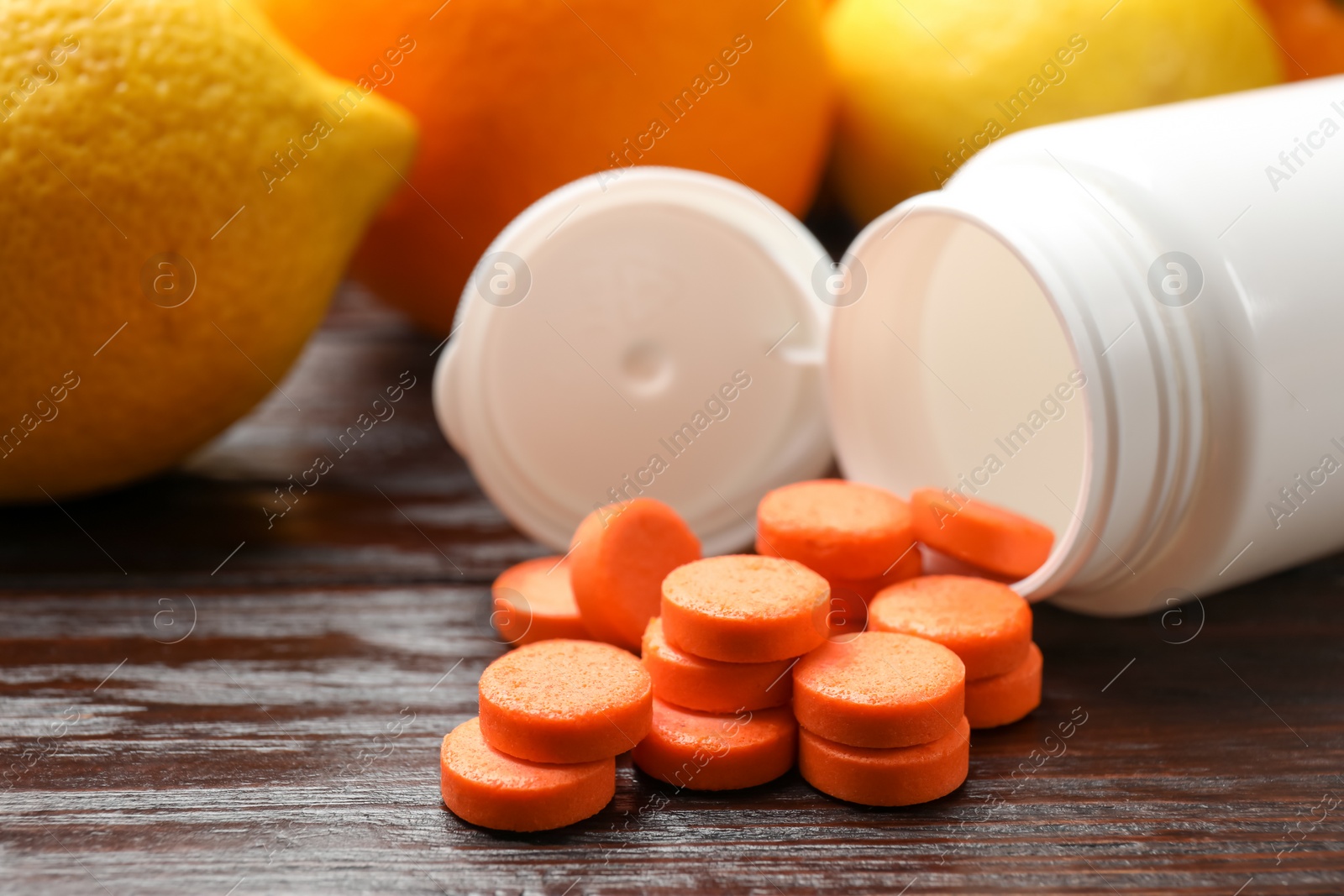 Photo of Dietary supplements. Overturned bottle, pills and fruits on wooden table, closeup