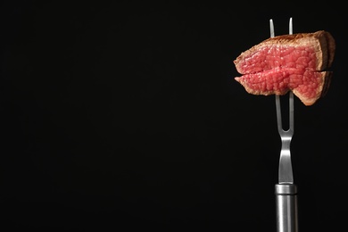 Carving fork with pieces of steak and space for text on black background. Tasty meat