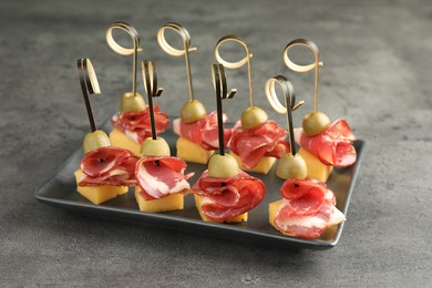 Tasty canapes with olives, prosciutto and cheese on grey table, closeup