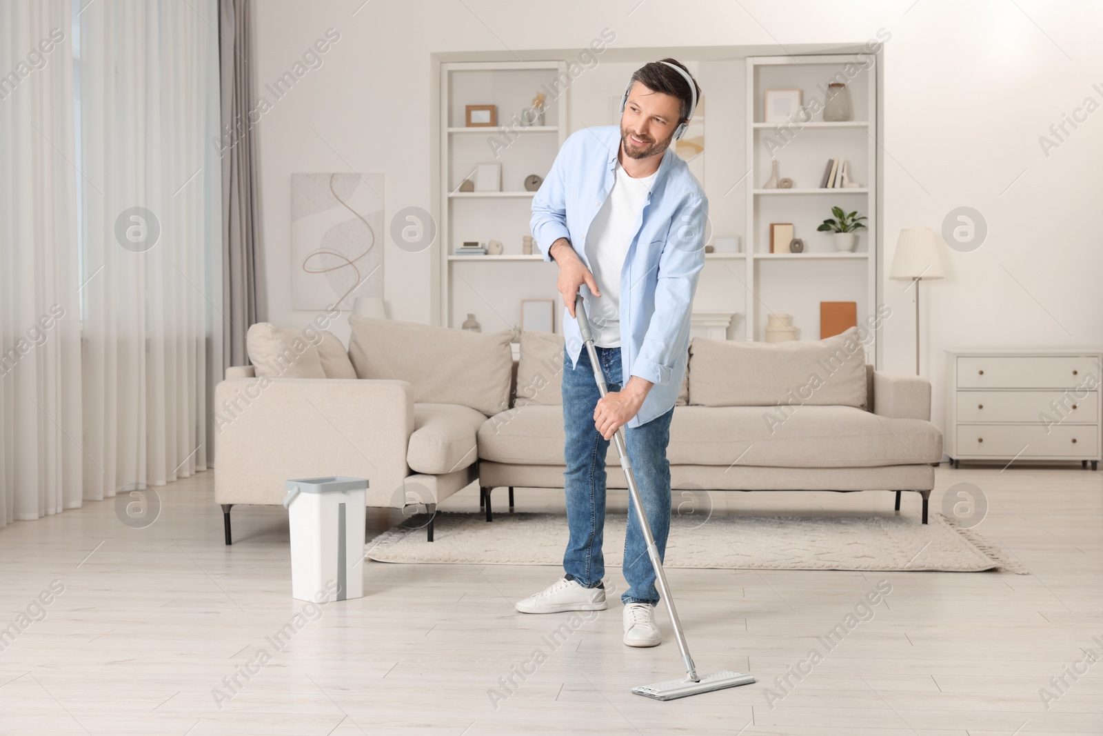 Photo of Enjoying cleaning. Man in headphones listening to music and mopping floor at home