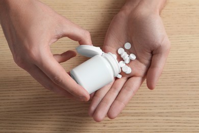 Photo of Man pouring pills from bottle at wooden table, top view