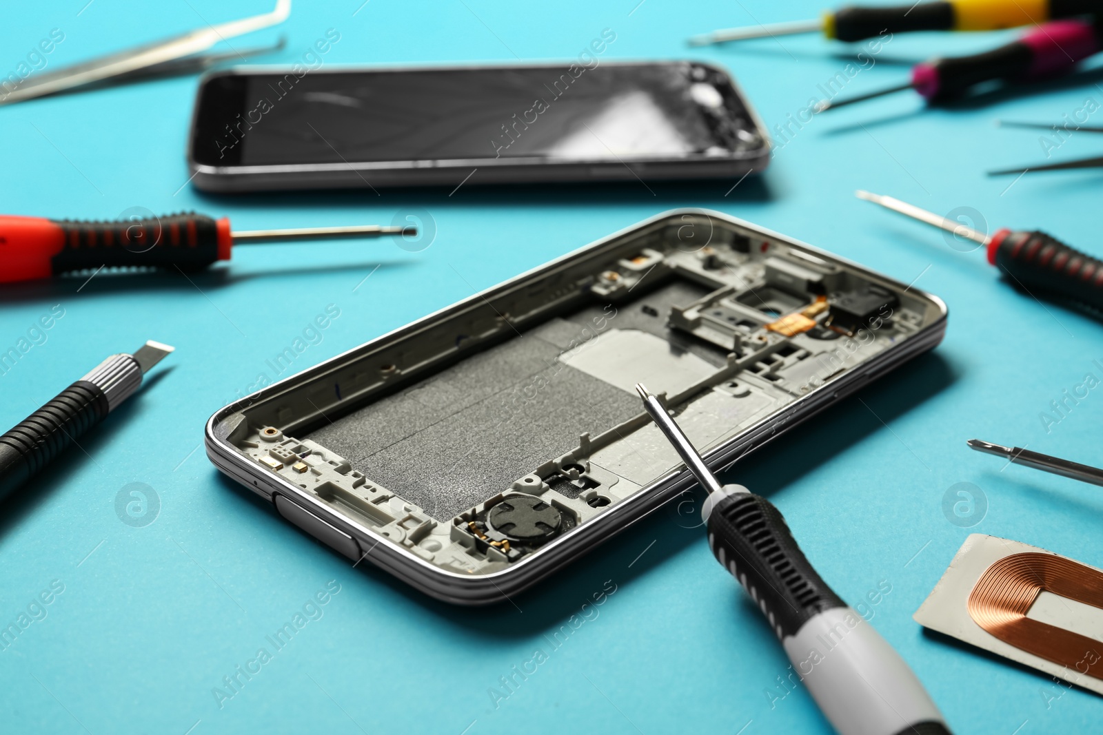 Photo of Damaged smartphone and repair tools on light blue background, closeup