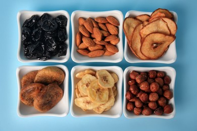 Bowls with dried fruits and nuts on light blue background, flat lay