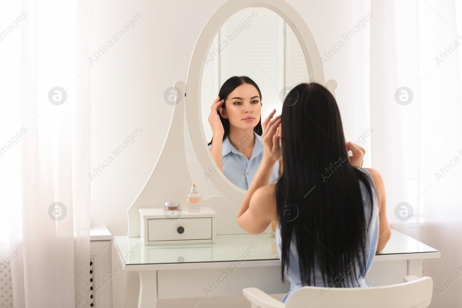 Photo of Beautiful young woman looking at herself in mirror indoors