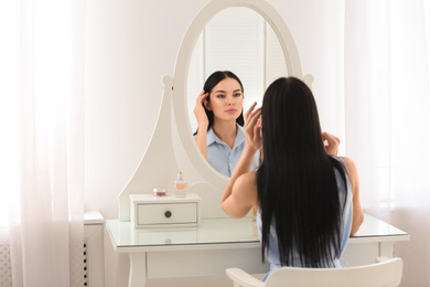 Photo of Beautiful young woman looking at herself in mirror indoors