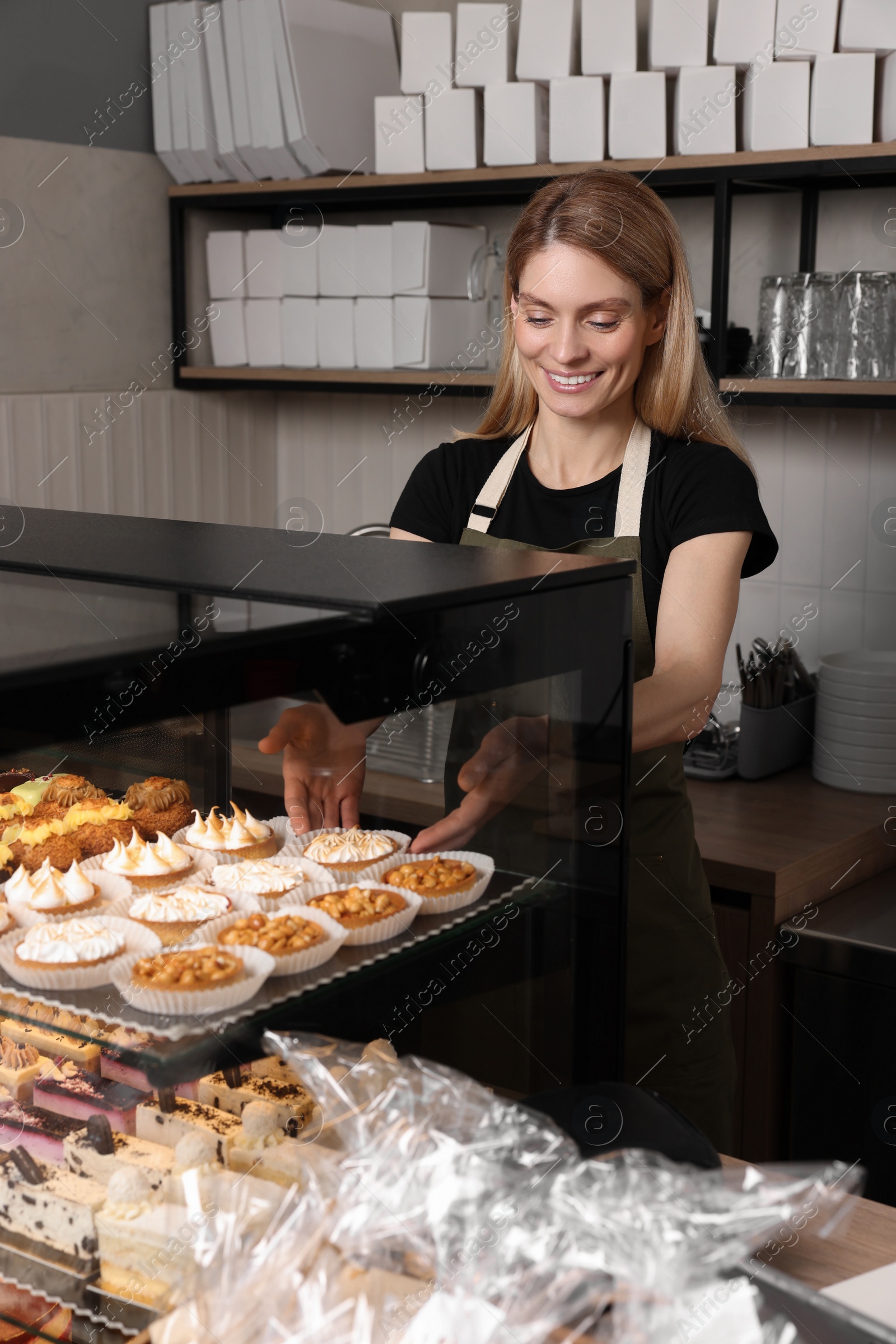 Photo of Happy seller taking delicious dessert from showcase in bakery shop