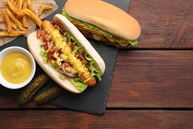 Photo of Delicious hot dogs with lettuce, onion and pickle served on wooden table, flat lay. Space for text