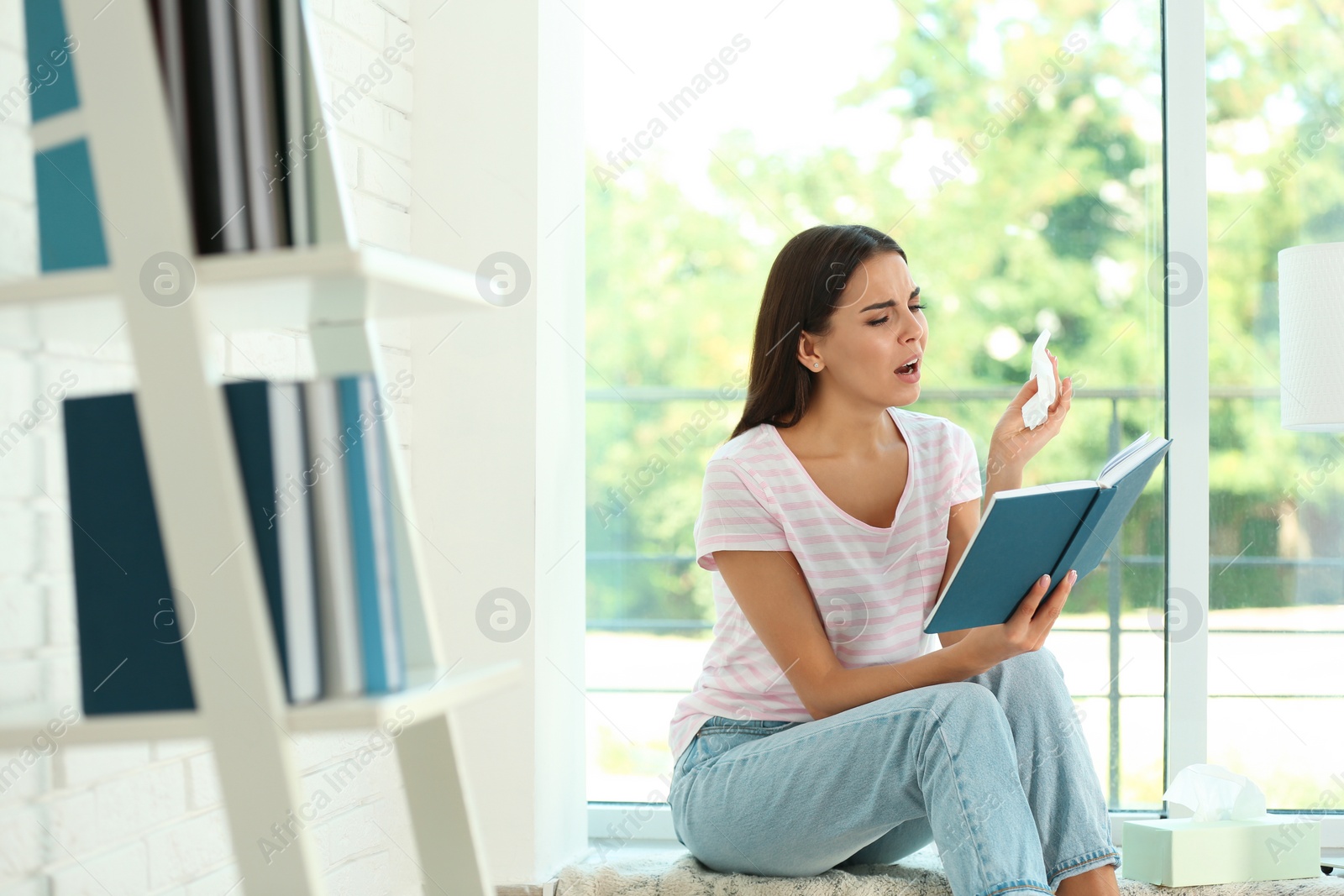 Photo of Young woman with book suffering from allergy at home