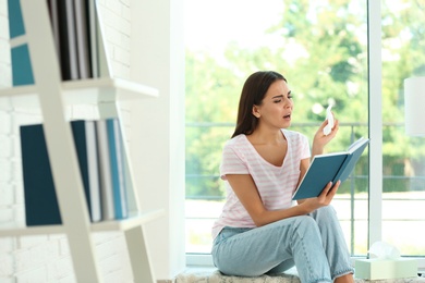 Young woman with book suffering from allergy at home