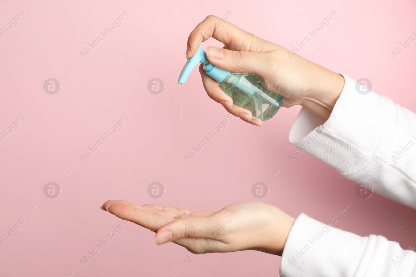 Photo of Woman applying antiseptic gel on hand against pink background, closeup