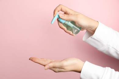 Photo of Woman applying antiseptic gel on hand against pink background, closeup