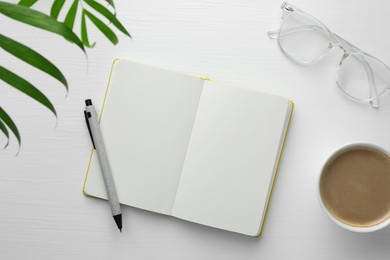 Open notebook, pen, glasses and cup of coffee on white wooden table, flat lay. Space for text