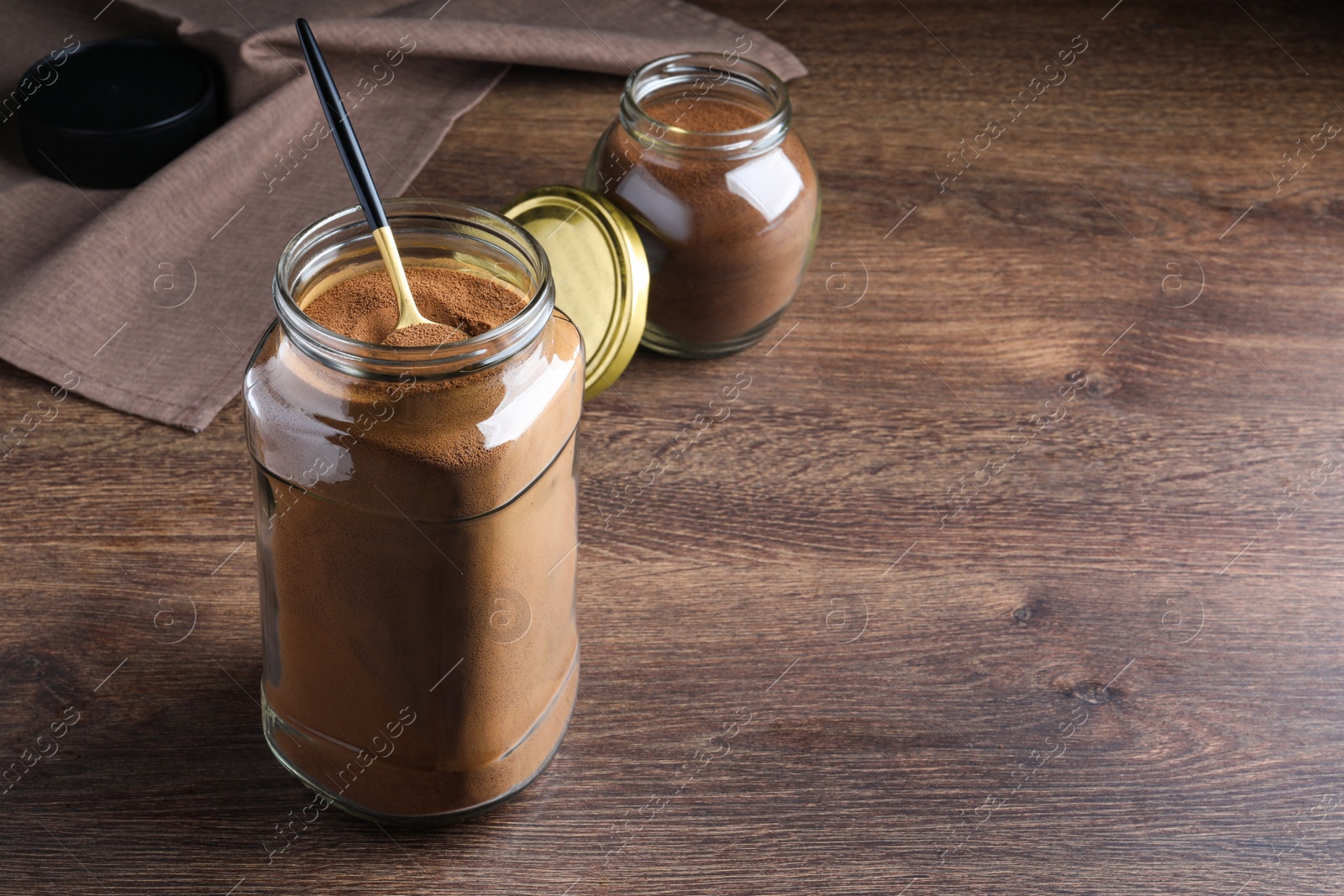 Photo of Jars of instant coffee and spoon on wooden table. Space for text