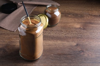 Jars of instant coffee and spoon on wooden table. Space for text