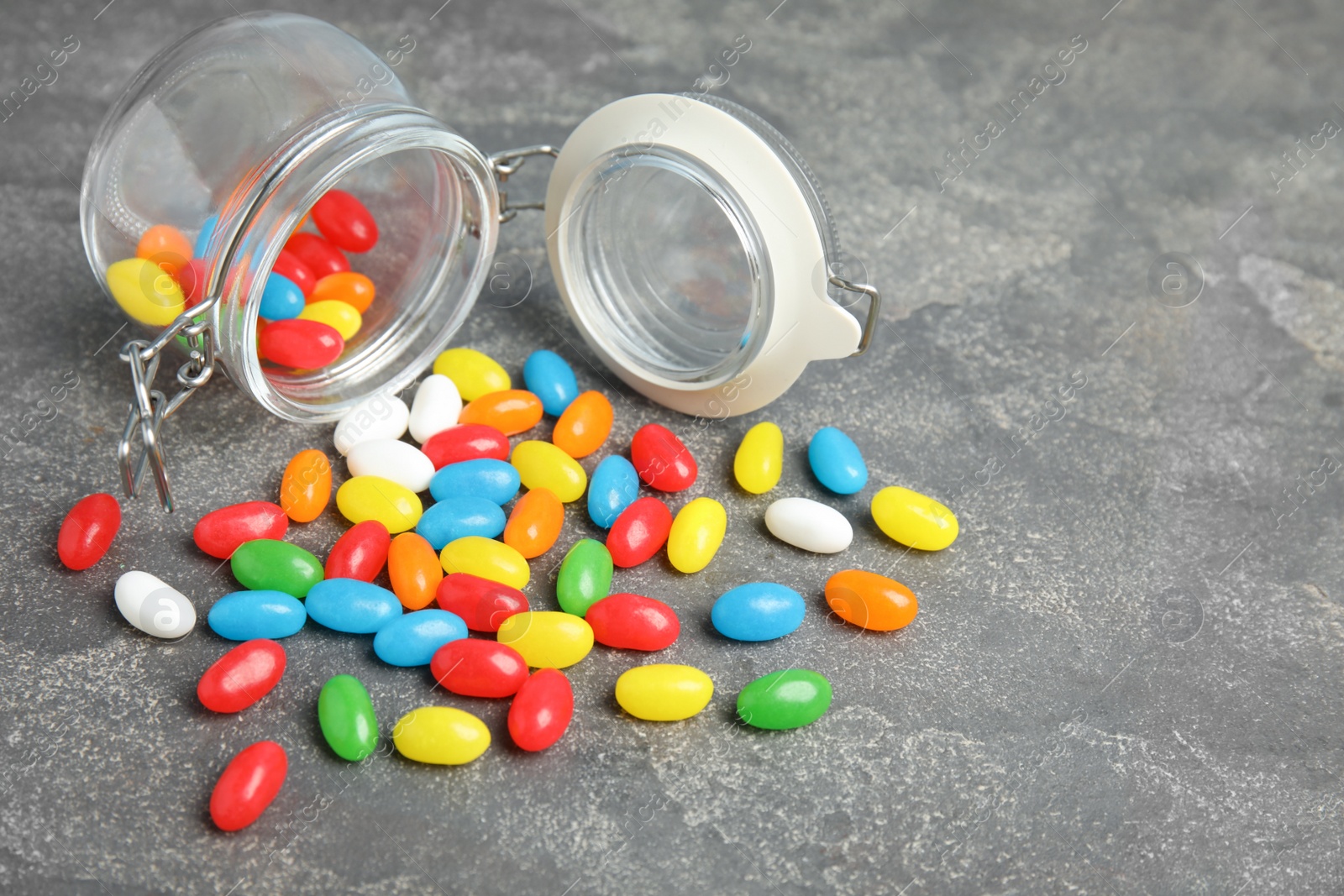 Photo of Overturned jar with jelly beans on stone background. Space for text