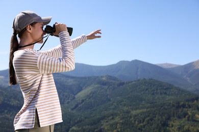 Woman looking through binoculars in mountains on sunny day