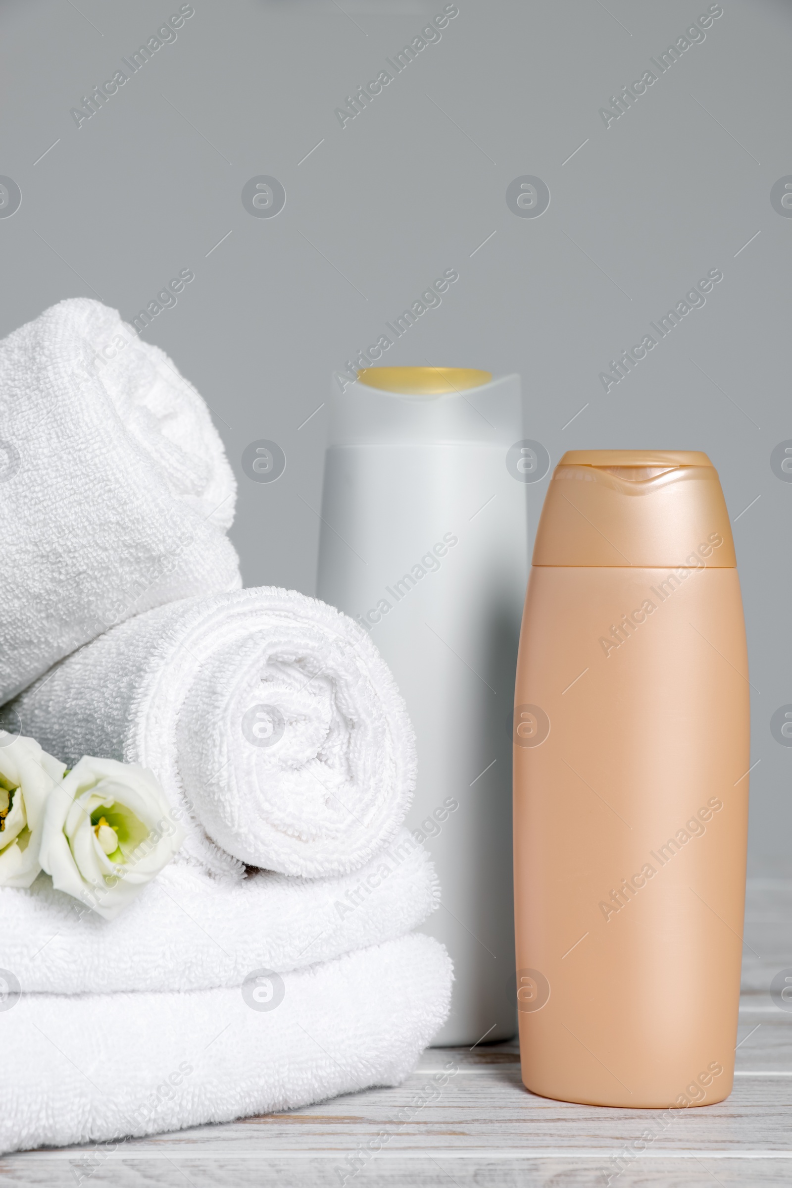 Photo of Soft white towels with flowers and cosmetic products on wooden table against grey background