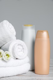 Photo of Soft white towels with flowers and cosmetic products on wooden table against grey background