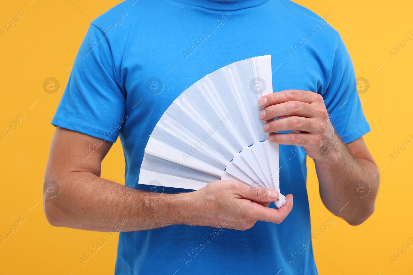 Photo of Man holding hand fan on orange background, closeup