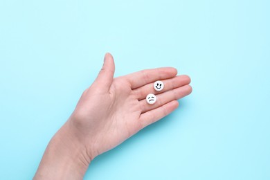 Woman holding antidepressants with different emoticons on light blue background, top view